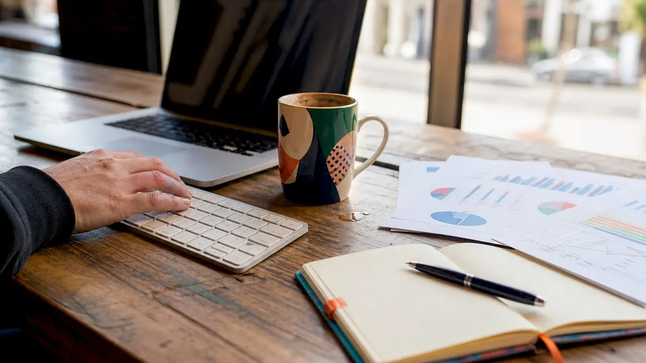 Hands typing on keyboard next to laptop with analytics reports